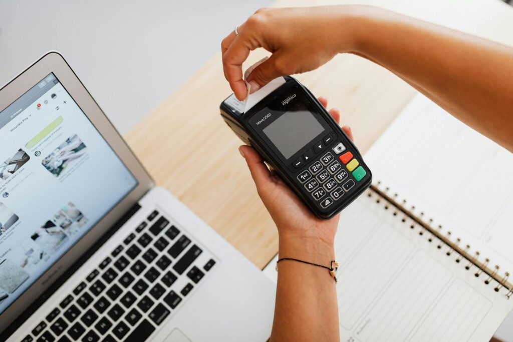 Person inserts a card into a handheld Ingenico payment terminal next to a laptop on a desk, completing a payment.