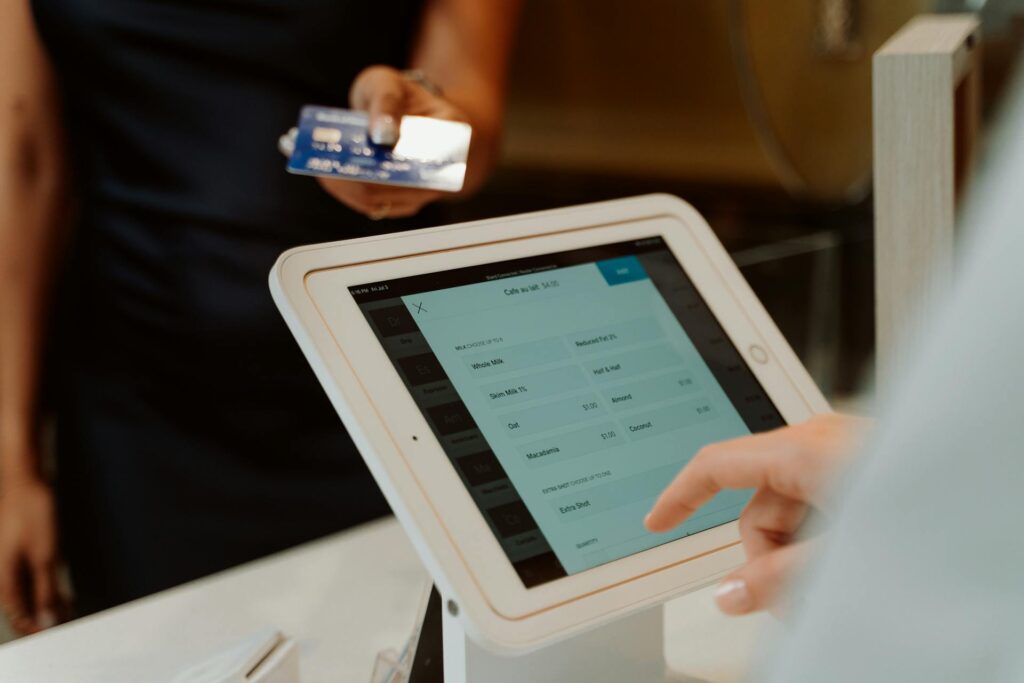 Person holds a blue credit card near a touchscreen point-of-sale tablet at checkout, preparing to pay.