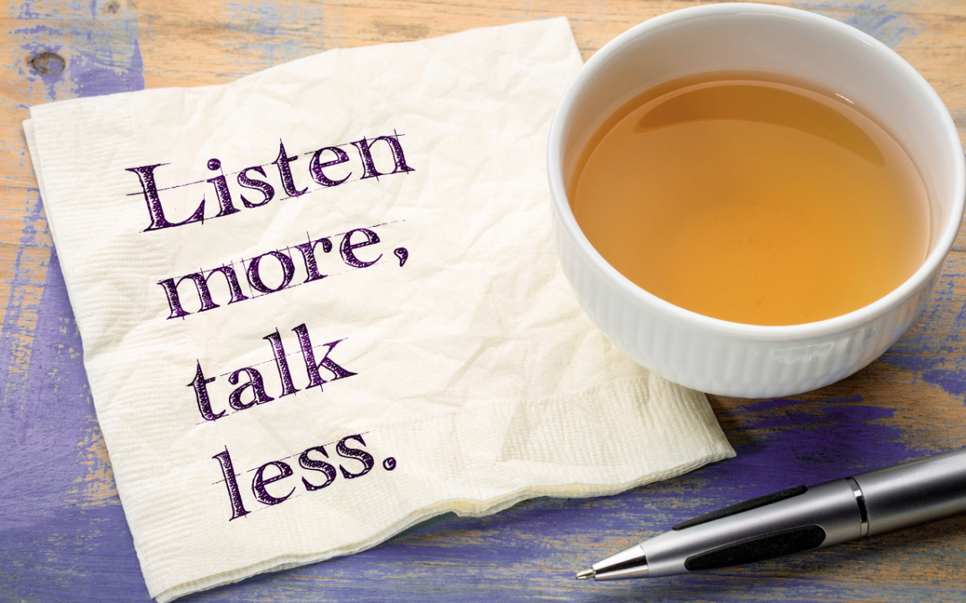 Napkin printed with 'Listen more, talk less.' beside a cup of tea and a pen on a wooden table.